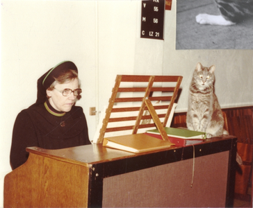 102053 Zuster Jeanne Verhoef met poes bij het harmonium