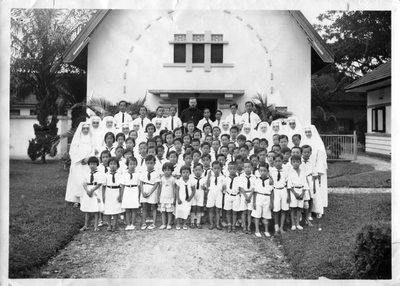 250352 Groepsfoto van pastoor Driessen, zusters en leerlingen voor het internaat van de congregatie te Tandjung Balai ...