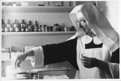 250357 Zuster Perpetua maakt een injectie klaar, vermoedelijk voor de polikliniek of het ziekenhuis van de congregatie ...