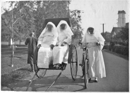 252286 Zuster Leontine met fiets naast een riksja met mère Isabelle en zuster Dorothea, in een straat te Medan op ...