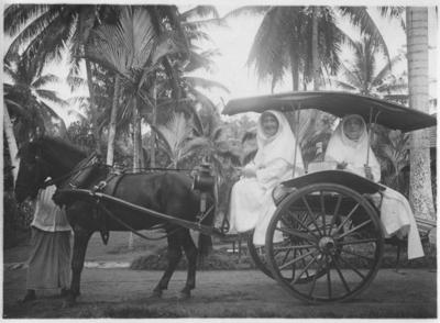 252293 Zuster Eligia achterop in een sado (rijtuig) en zuster Henriëtte op de plaats van de koetsier, Indonesië
