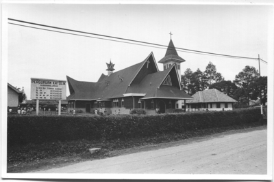 252309 De kerk (uit 1956), rechts daarvan de pastorie (uit 1953) en links een deel van de SKP (Sekolah Kepandaian ...