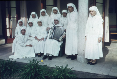 178354 Zusters luisteren naar het accordeonspel in het klooster te Deli Tua (Indonesië)
