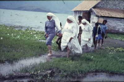 178382 Na een flinke regenbui te Pangururan moeten de zusters met opgehouden jurken door de plassen lopen (Indonesië)