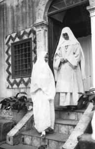 116132 Witte Zuster met Noord-Afrikaanse vrouw voor de ingang van een klooster in Algerije
