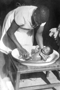 116142 Een leerling-verpleegster wast een baby te Sumwe, Tanganjika (Tanzania)