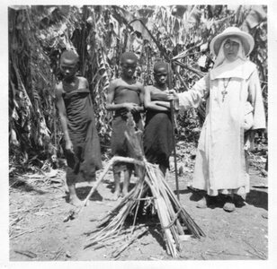 116176 Zuster Coletta met drie meisjes bij een offerhuisje voor geesten in een bananentuin in het binnenland van Tanzania