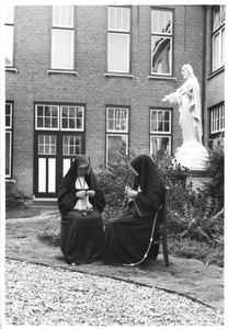 122184 Twee zusters recreëren met handwerk bij het H. Hartbeeld op de binnenplaats van het moederhuis St. Jozef te Amersfoort