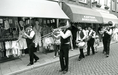 BR_VOORSTRAAT_553 Tijdens de Kolder Koopavond loopt een fanfare door de Voorstraat langs de boekhandel; 9 augustus 1984