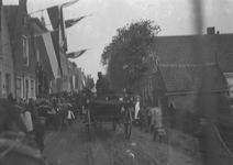 A1022 Feestelijke optocht met een paard met wagen en een muziekvaandel. Aan de gevels van de huizen hangen vlaggen.