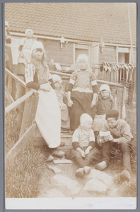 WAT001001993 Vrouw en kinderen in klederdracht, poserend op een trap. Rechts hangen ankers.