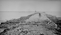 336 - 'Levensstrijd'. Man loopt over houten planken over de caissons op dijk in aanbouw