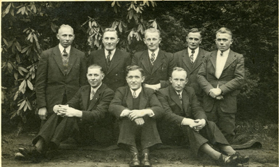 135 - Groepsfoto van acht mannen voor een struik