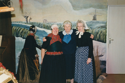N 8058 - drie vrouwen voor paneel met winterlandschap; links een pop in oude dracht met oorijzer; vlnr: Gerrie Rekers; ...