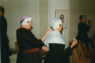 N 8062 - vrouw links, oude dracht uit de rouw, helpt vrouw, oude dracht in zware rouw; bij het plooien van de witte ...