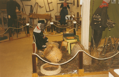 N 8122 - beeld van opstelling in oudheidkamer; achtergrond: boerenwerktuigen; midden voor: imker met korven; rechts ...