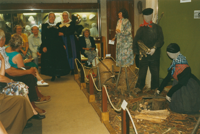 N 8128 - klederdrachtshow in de oudheidkamer; vrouw rechts: Alie de Graaf; vrouwen in dracht: links Nel van de Berg; ...