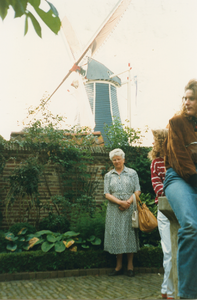 N 8137 - vrouw poseert tegen muur met daarachter de kap van een molen; rechts voor jonge vrouw op stenen muurtje; ...
