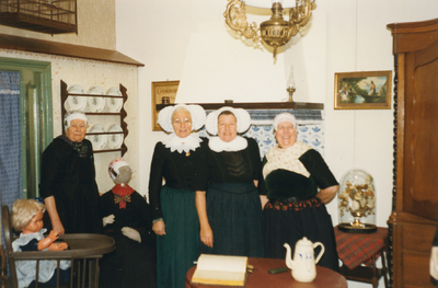 N 8140 - vier vrouwen, in dracht, staan bij een pop in tipmutsdracht; op visite bij opoe Grietje; vrouwen vlnr: Fenna ...