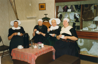 N 8141 - achtergrond vitrine met diverse delen van de klederdracht; nog even koffiedrinken in de koffiehoek; vlnr: ...
