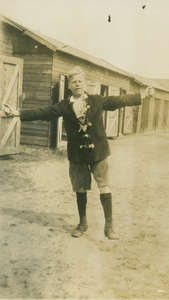 9982 - Jongeman met uitgestoken armen voor enkele barakken