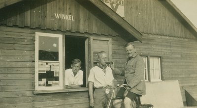 9990 - Winkel met drie man, waarvan één op de fiets