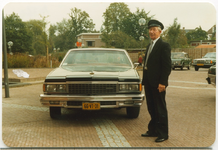 14364 - Chauffeur dhr. K. Bruijnes poseert op een plein bij een zwarte Chevrolet (met het kenteken 66-VT-31)