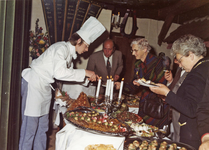 7076 - De gasten laten zich verwennen door het nuttigen van een buffet. De kok helpt hen daarbij. Aan het buffet staan ...