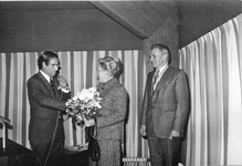 7097 - Burgemeester Veen overhandigt een bos bloemen aan mevrouw Roelofsen. De heer Roelofsen heeft een zilveren pauw ...
