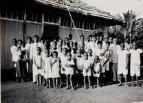 95 Zuid N. Guinea. De gemeente Toeray, vergaderd voor het schoolgebouw. De schoolkinderen zien er behoorlijk gekleed ...