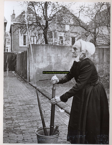F002967 Juffrouw Beijer, J. in door-de-weekse Kamper klederdracht aan het glazenwassen.