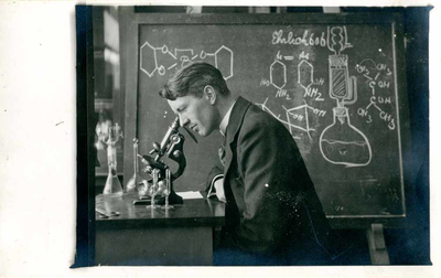 F009528 Uit het fotoalbum van de fam. Berk.Johannes Berk (geb. 4 jul 1897) kijkend door een microscoop tijdens zijn ...