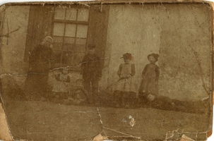 F010855 Echtpaar in klederdracht met vier kinderen poseren voor het huis, opschrift op de achterzijde van de foto: ...
