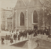 F000459 Kerkgangers verlaten de Broederkerk richting huis via de Burgwal en de Broederbrug, links van de kerk staat de ...