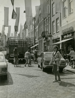F010250 De Oudestraat ten tijde dat er nog auto's mochten rijden, een vrouw die de straat oversteekt, twee fietsende ...