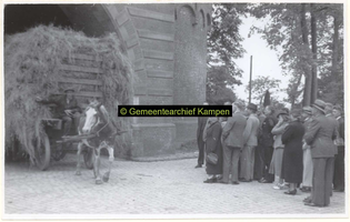 F006290 Burgemeester H.M. Oldenhof en een gezelschap kijken naar een paard en wagen met hooi, die onder de ...