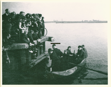 F008648 Kampen in oorlogstijd. Een groep Kampenaren kijkt toe hoe een 6-tal mannen in een bootje aan de IJsselkade stapt.