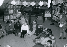 F010986 Kinderen in een kring in de boekwinkel/bibliotheek tijdens de Kinderboekenweek.