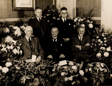  Groepsfoto van het bestuur van de Spaarbank te Vianen, te midden van bloemstukken in het kantoor, ter gelegenheid van ...