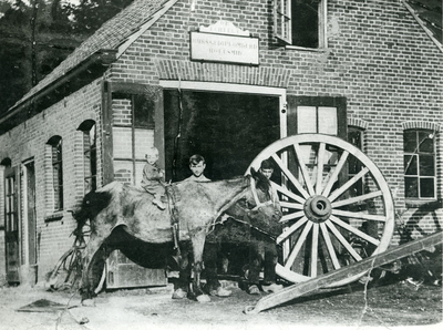  Smederij Van Echtelt. Op de voorgrond een kind op een paard, twee medewerkers en een wagenwiel van een mallejan.