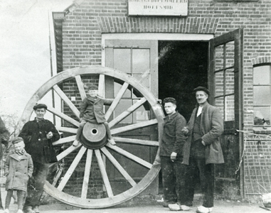  Smederij Van Echtelt. Op de voorgrond een wagenwiel van een mallejan met van links naar rechts: Theo van Echtelt, J. ...