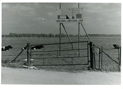  Een weiland met koeien met een bouwbord met de tekst 'HIER KOMT het DORPSHUIS van ODIJK'.