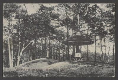  Bosgezicht met een rond de stam van een boom gebouwde paddenstoel, daaronder een ronde bank.