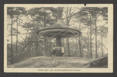  Bosgezicht met een rond de stam van een boom gebouwde paddenstoel, daaronder een ronde bank met twee dames.