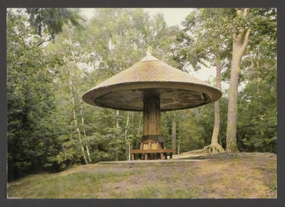  Bosgezicht met een rond de stam van een boom gebouwde paddenstoel met daaronder een ronde bank.
