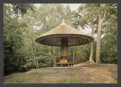  Bosgezicht met een rond de stam van een boom gebouwde paddenstoel met daaronder een ronde bank.