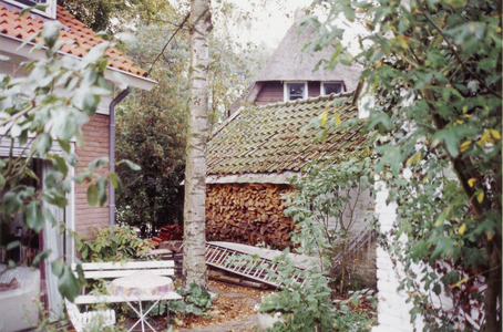  Zijkant huis met opgestapeld hout en tuinzitje.