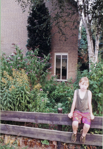  Zijkant huis met tuin en kind op hek.