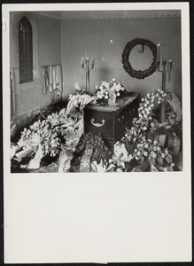  In het mausoleum ligt op de kist een bloemstuk van de kleinkinderen. Links op de muur hangen de linten van de ...
