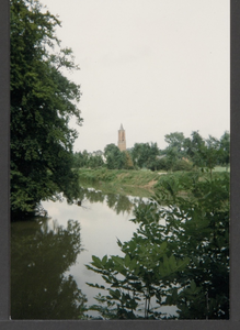  Water omgeven door veel bomen en overige beplanting, in de verte de toren van de St. Andrieskerk.